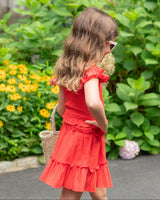 Young girl in a red dress standing among flowers and greenery