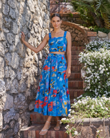 Woman in a blue floral dress standing against a stone wall with flowers in the background