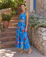 Woman in a blue floral dress standing outdoors near stone steps and plants.