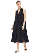 Model looking to the side wearing a black sleeveless, high neck with ruffle detail, buttoned shirt dress with black sandals