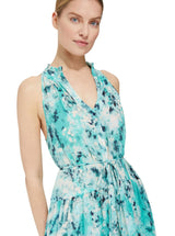 Close up and detailed shot of model wearing an ocean color, sleeveless, high neck with ruffle detail, buttoned shirt dress with optional matching belt with tassels and pockets. 