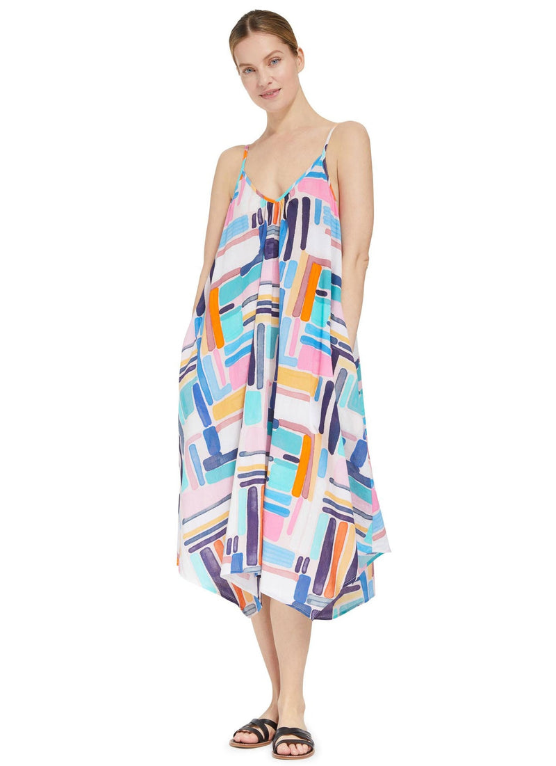 Model posing with hands in her pockets wearing a geometric and graphic colored strappy and long flowy dress with adjustable back shoulder straps, v-neckline front pockets with black sandals