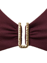Detail of hammered gold hardware on burgundy bikini top and white background