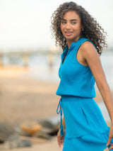 Model wearing a light blue dress with an elastic waistband, adjustable drawstring and a V-notch neckline with a ruffled skirt and pockets