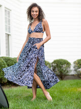 Model in backyard smiling and wearing a black and white leopard print midi length skirt with side slits and elastic waistband with drawstring detail with matching v-neck bikini top 