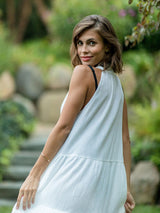 Model looking over her shoulder grinning wearing fresh white sleeveless, high neck with ruffle detail, buttoned shirt dress. 