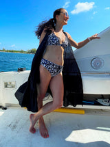Women on a boat wearing a black and white leopard print plunge neckline, classic bikini top with adjustable straps and an elastic underband with matching midrise bottoms and a black flowy duster dress