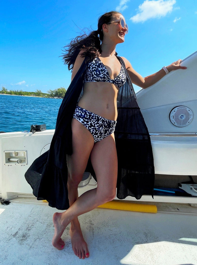Women standing on a boat wearing a black and white leopard print plunge neckline, classic bikini top with adjustable straps and an elastic underband with matching midrise bottoms and a black flowy duster dress