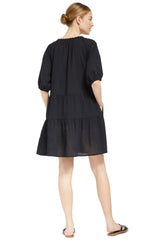 the back of a model wearing a black slightly above the knee dress with rounded neckline and short puff sleeve with a covered elastic cuff 
