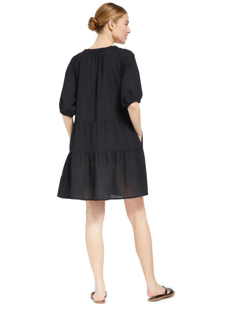 the back of a model wearing a black slightly above the knee dress with rounded neckline and short puff sleeve with a covered elastic cuff 