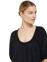 close up shot of a model wearing a black slightly above the knee dress with rounded neckline and short puff sleeve with a covered elastic cuff 