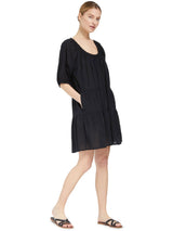 model posing with her hands in her pockets wearing a black slightly above the knee dress with rounded neckline and short puff sleeve with a covered elastic cuff with black sandals 