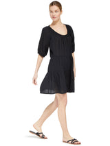 model wearing a black slightly above the knee dress with rounded neckline and short puff sleeve with a covered elastic cuff with black sandals 