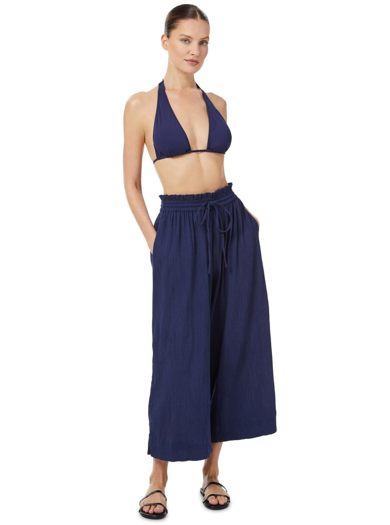 Model wearing a navy triangle bikini top with halter neck tie, adjustable cups, and a spaghetti tie under the bust with matching beach pants