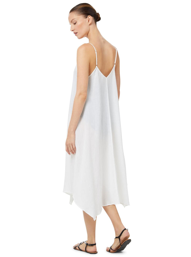 model looking over her shoulder wearing a fresh white strappy and long flowy dress with adjustable back shoulder straps, and v-neckline front and back with pockets with black sandals. 