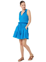 Model posing with hands in her pockets and looking to her side wearing a grotto blue (light blue) dress with an elastic waistband, adjustable drawstring and a V-notch neckline with a ruffled skirt and pockets