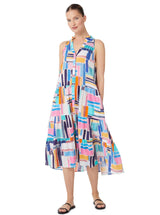 Model smiling and wearing a geometric and graphic colored sleeveless, high neck with ruffle detail, buttoned shirt dress with optional matching belt with tassels and pockets.. 
