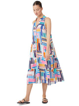 Model looking down and wearing a geometric and graphic colored sleeveless, high neck with ruffle detail, buttoned shirt dress with optional matching belt with tassels and pockets.. 