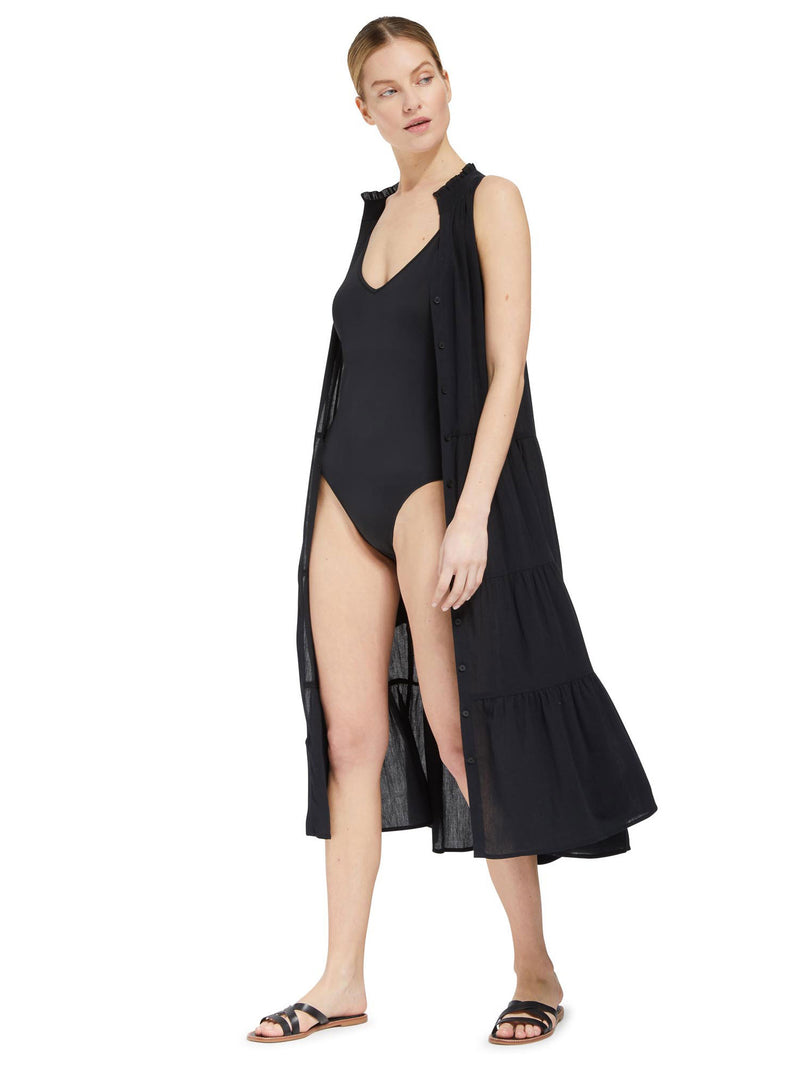 Model wearing black v-neckline one piece bathing suit with adjustable back straps with black duster dress and black sandals