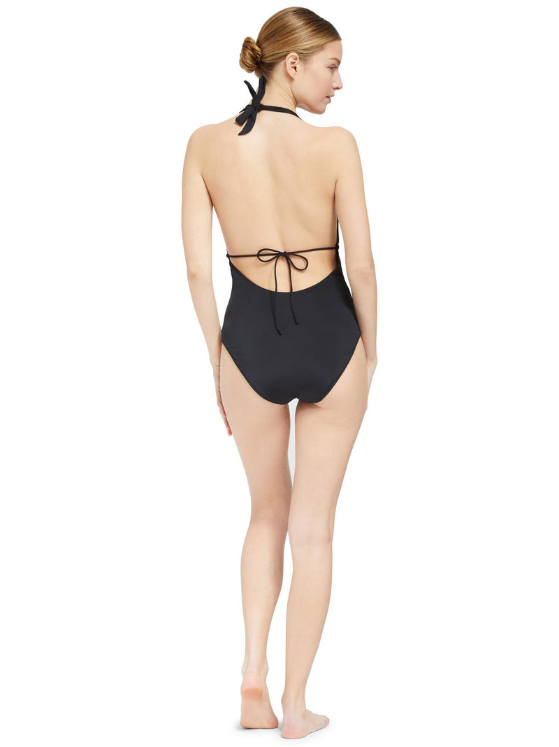 the back view of Model wearing black deep plunged one piece swimsuit with an adjustable halter-neck tie and under-bust string 